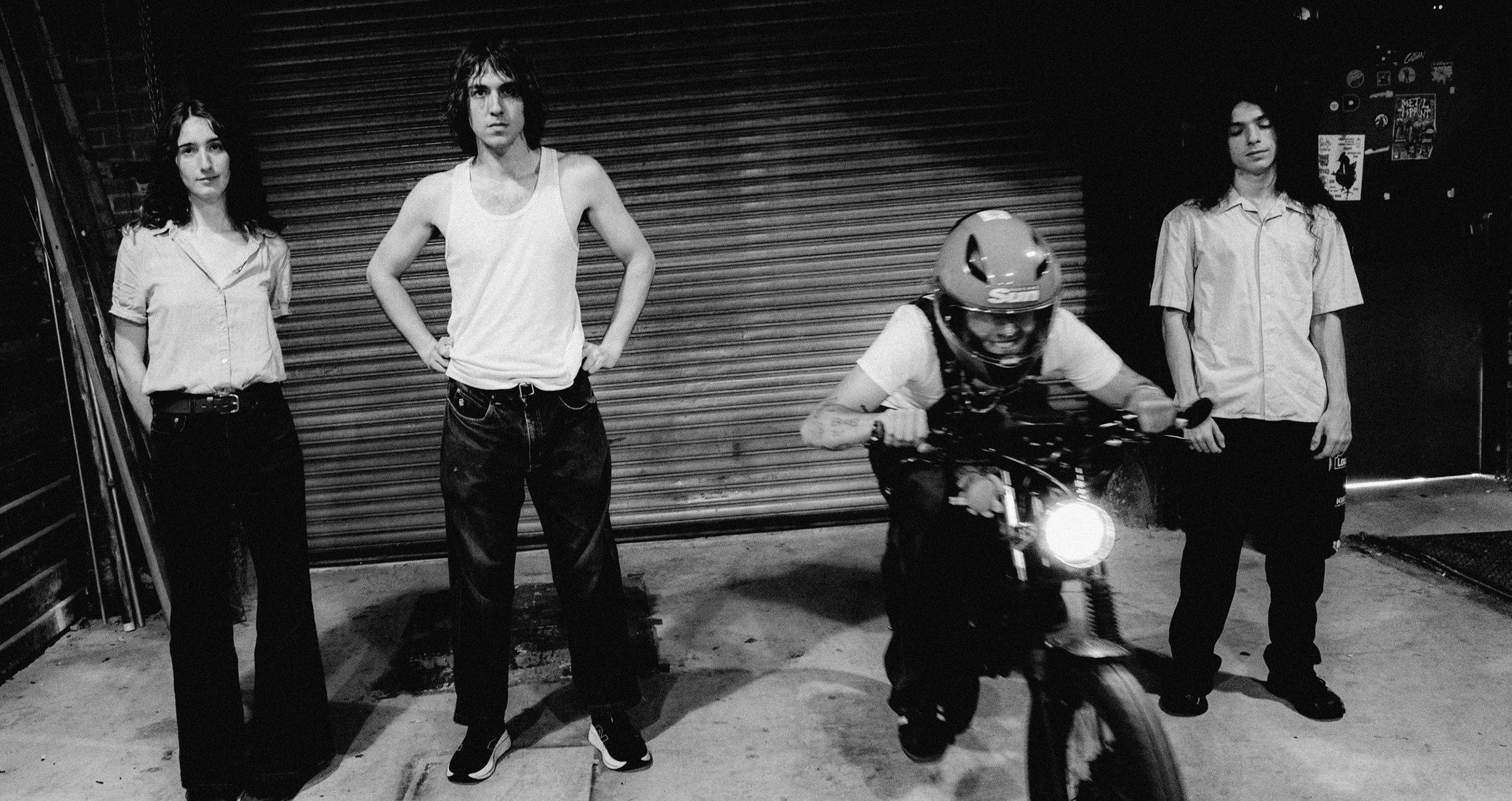 Schwarz Weiss Bild von vier Personen, eine auf einem Motorrad, vor Garagentor stehend