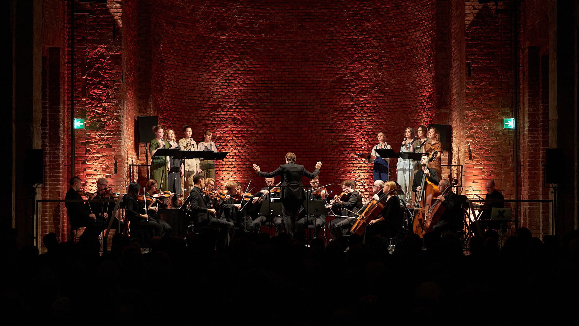 Ein Orchester vor einenr Bühnenkulisse aus rohen Ziegeln in warmem Licht