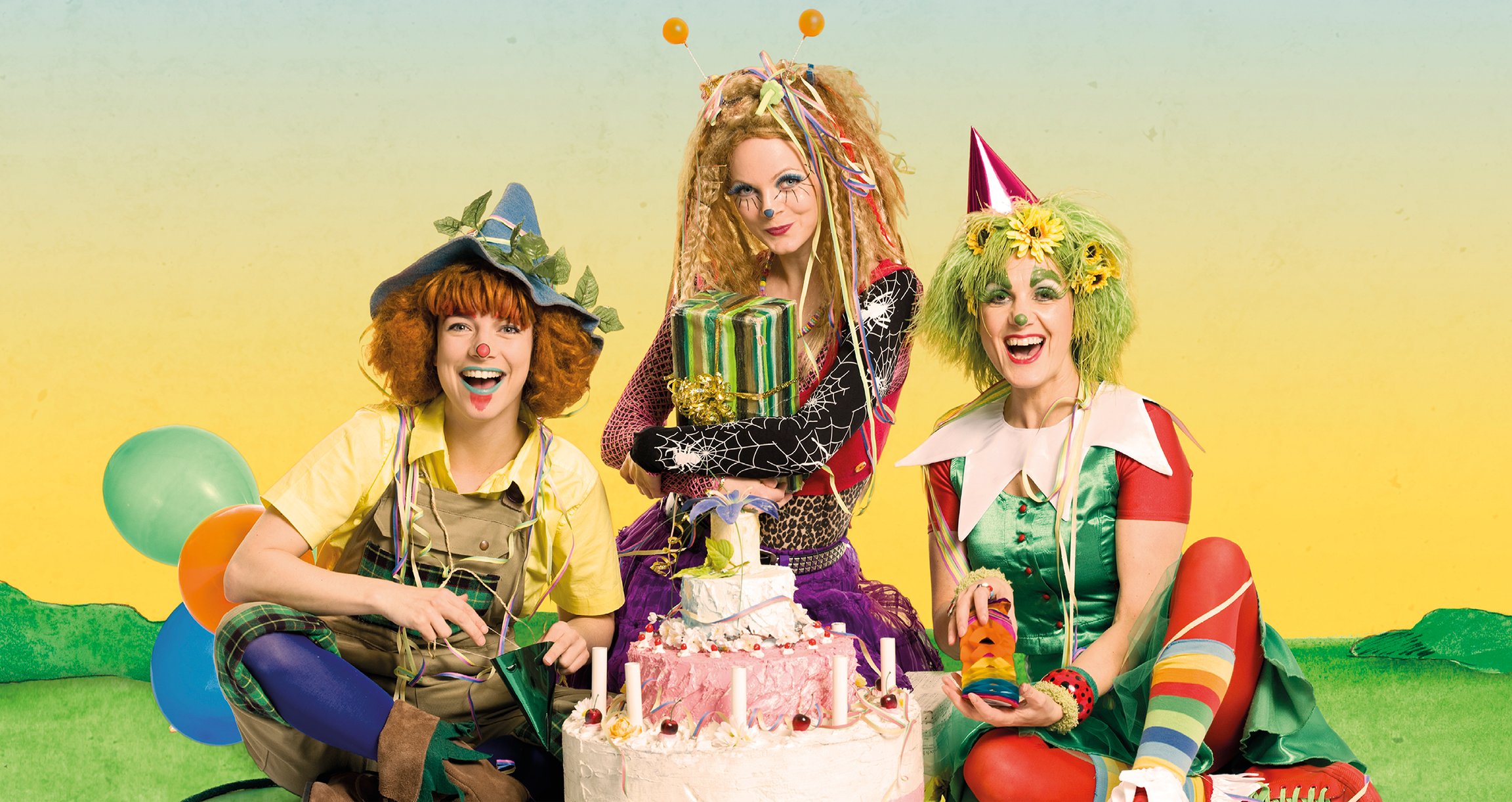 ein Bild von drei als Clowns verkleideten Mädchen mit einer Torte, Luftballons und Geschenken, auf gelbem Hintergrund