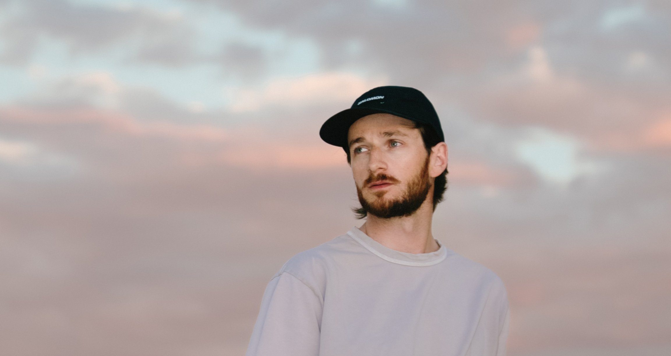 der Künstler mit einer schwarzen Mütze und einem Himmel mit rosa Tönen im Hintergrund.