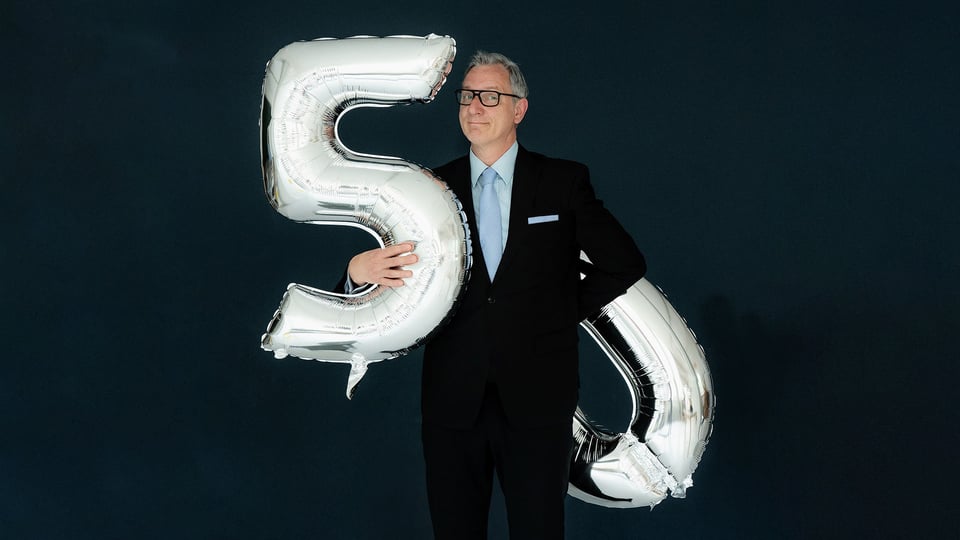 Foto für die Veranstaltung von Hans Gerzlich mit dem Künstler und Geburtstagsballons in der Form der Zahlen 5 und 0, vor einem dunkelblauen Hintergrund