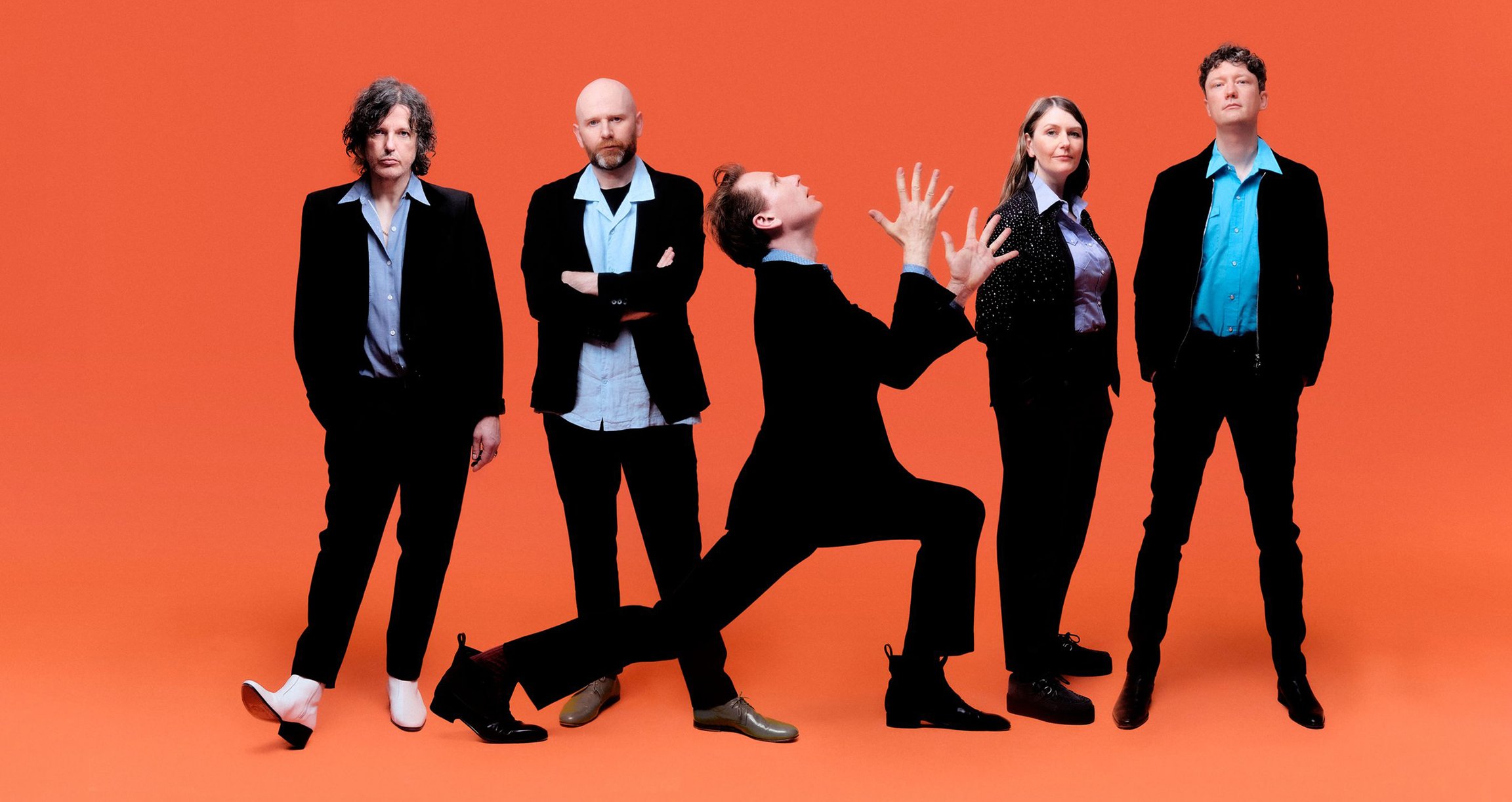 Franz Ferdinand in Anzügen vor einem orangenen Hintergrund
