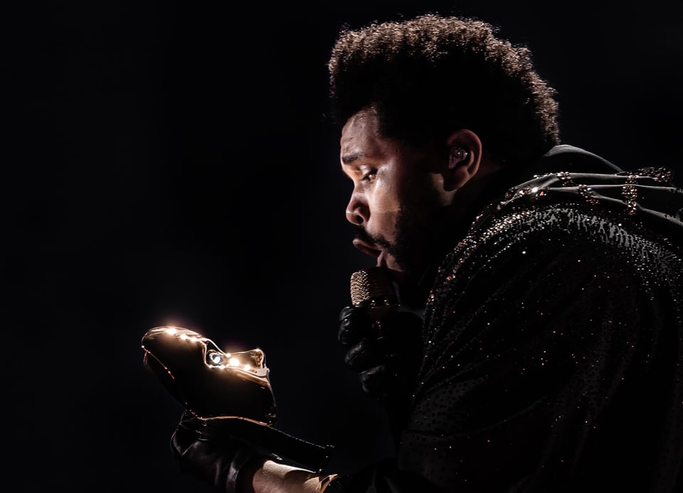 Foto des Künstlers THE WEEKND mit einer Maske in der Hand, die er vor schwarzem Hintergrund betrachtet