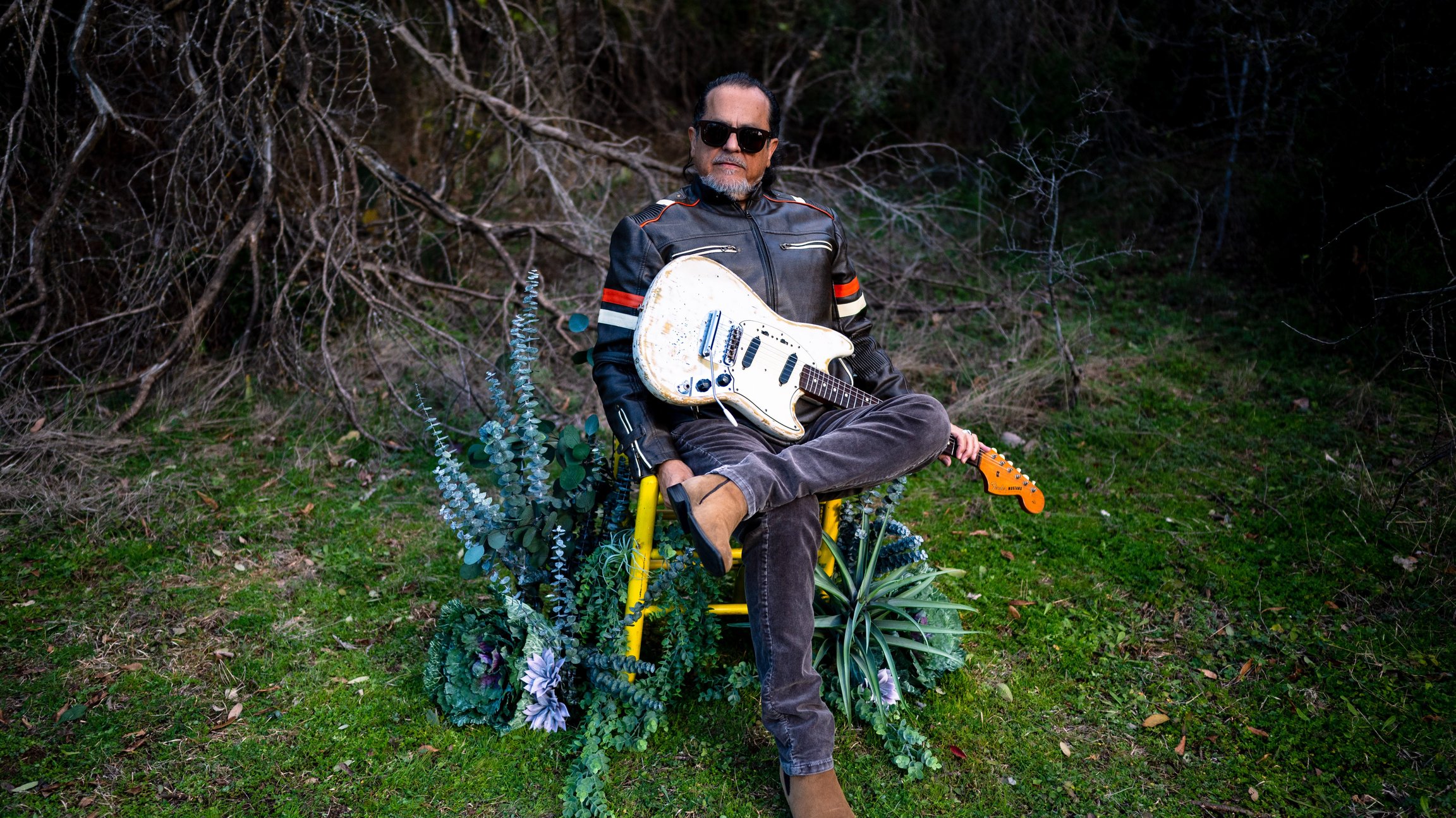Ein Mann mit Gitarre sitz auf einem Stuhl im Wald