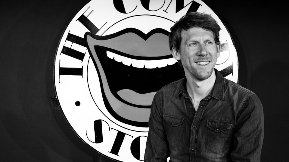 Christian Schulte Loh sitzt vor einem großen runden Logo mit einem stilisierten offenen Mund und dem Schriftzug THE COM… STORE