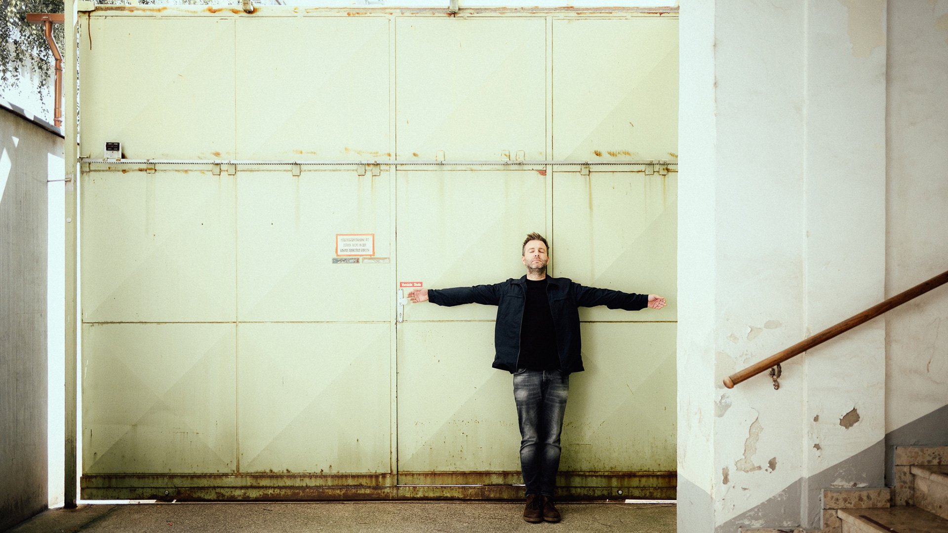 Foto für die Veranstaltung JOSH. solo – Wer singt dann Lieder für dich? mit dem Künstler und einer großen grünen Metalltür im Hintergrund