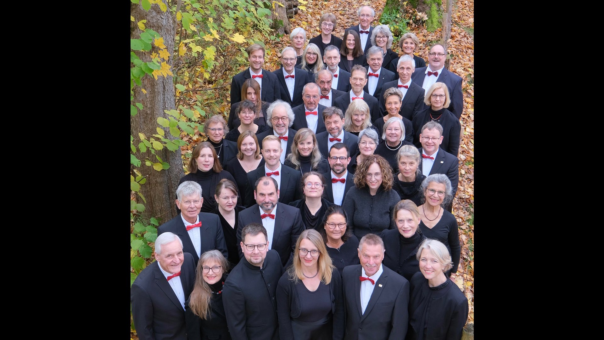 Der Chor in dunkler Kleidung in einem Laubwald stehend