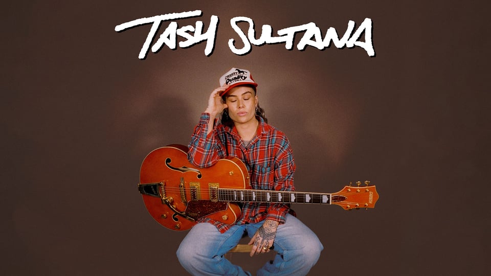 Eventfoto „TASH SULTANA“ mit der Künstlerin auf einem Hocker mit Saiteninstrument vor braunem Hintergrund.