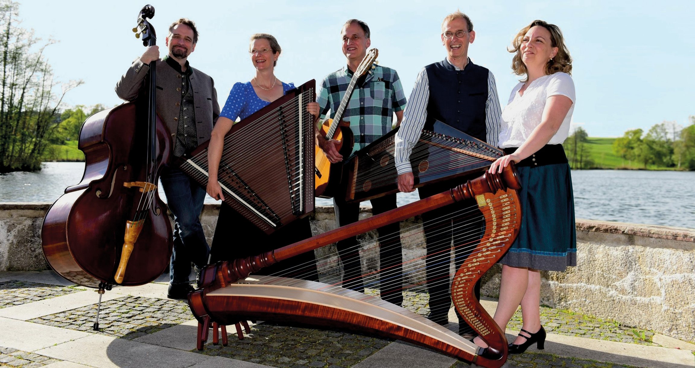 Die Musiker*innen mit ihren Instrumenten in der Hand vor einem Gewässer