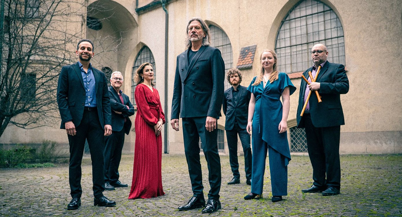 Sechs Personen, vier Herren in dunklen Anzügen und zwei Damen in farbigen Kleidern in historischem Innenhof