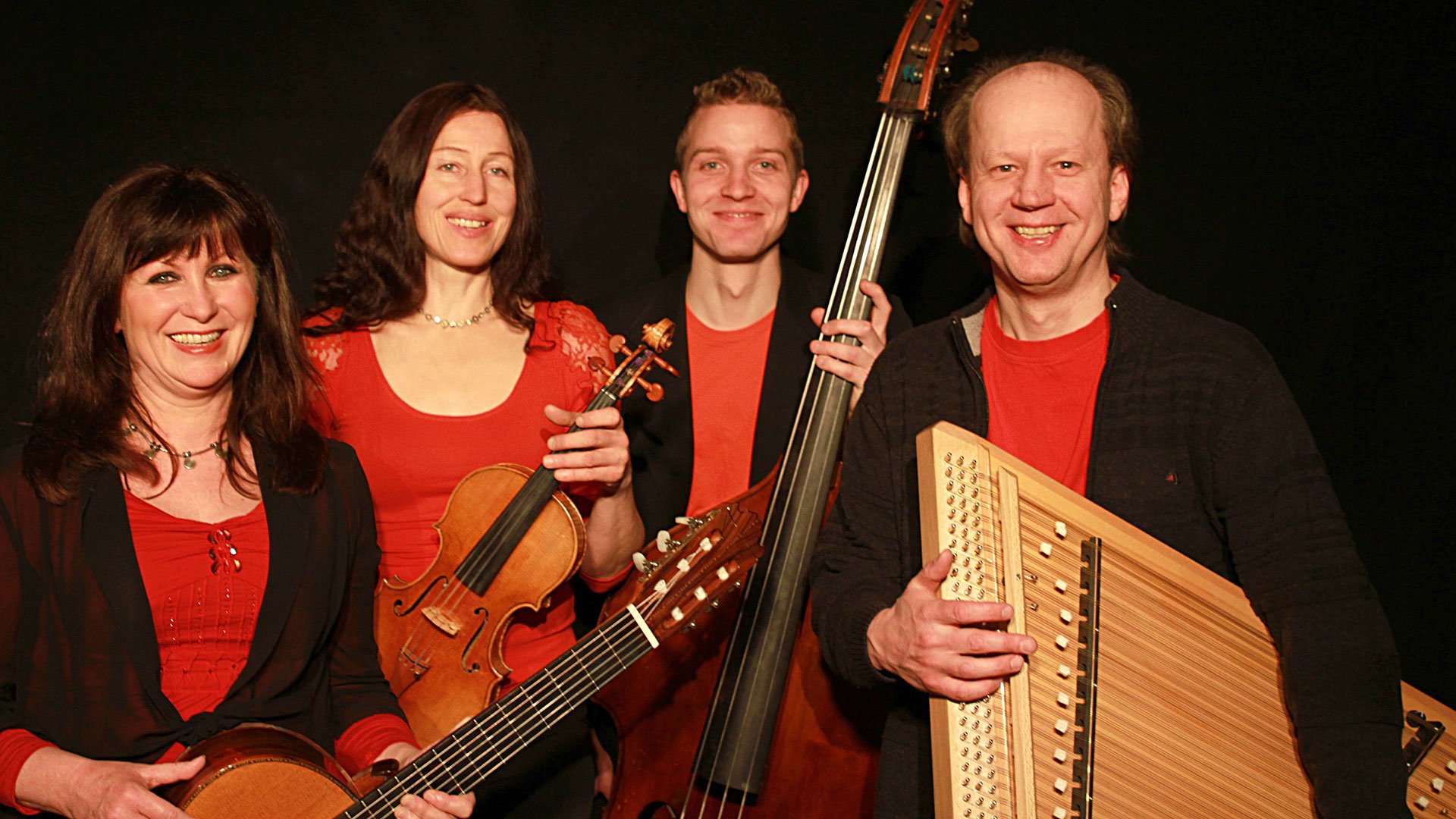 Welt-Weihnachtskonzert Rudi Zapf & Freunde: Vier Musiker mit Violine, Kontrabass, Gitarre und Hackbrett stehen nebeneinander vor schwarzem Hintergrund.