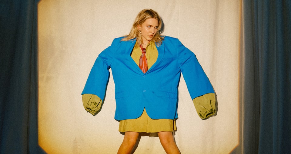 Dame in übergroßem blauem Sakko und Kravatte auf Bühne