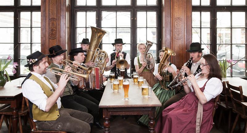 Neun Personen in Tracht mit Blasinstrumenten sitzen an Tisch mit Bierkrügen