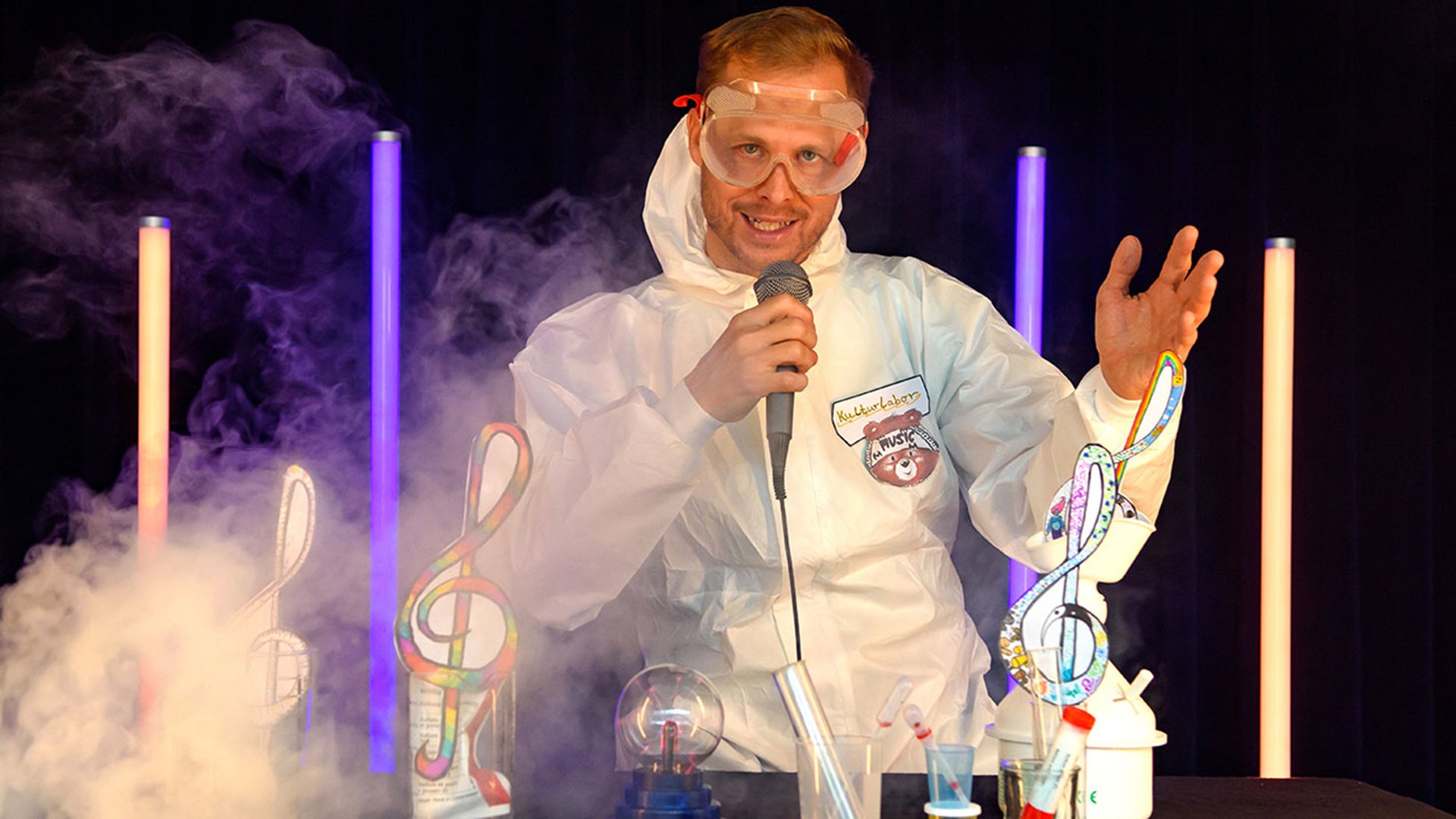 EIn Mann in weißem Overall und Schutzbrille und Mikrofon zwischen Leuchtstäben