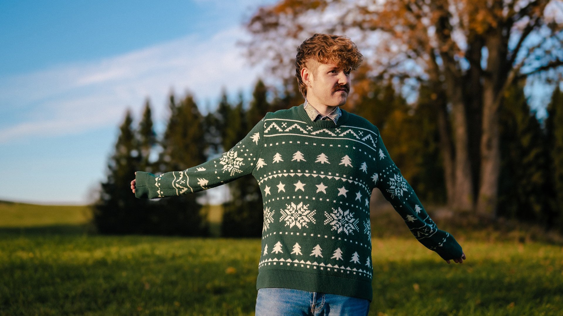 Benedikt Mitmannsgruber steht mit grünem Pulli auf einer Wiese bei Sonnenschein 