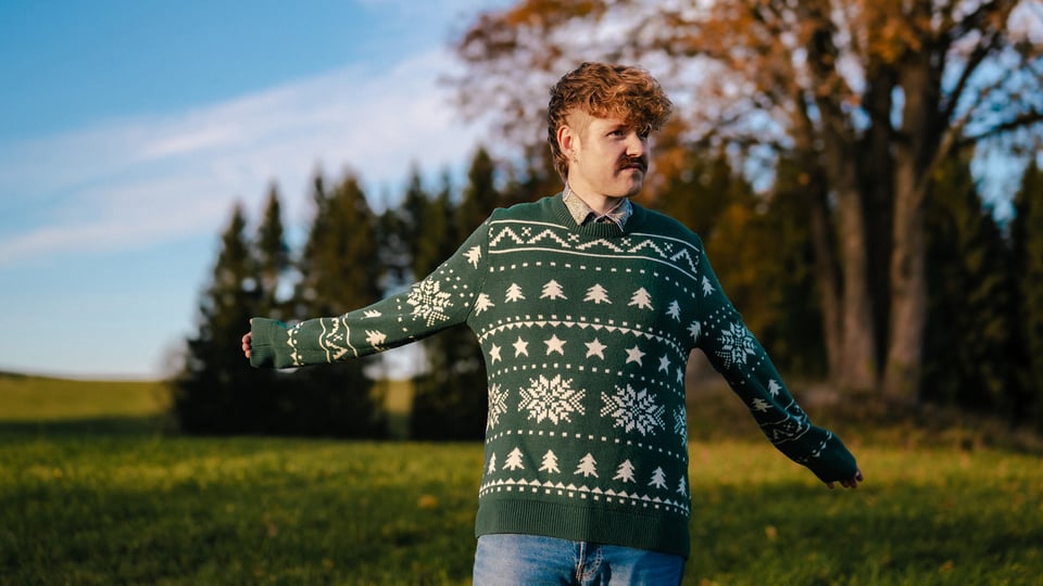 Benedikt Mitmannsgruber steht mit grünem Pulli auf einer Wiese bei Sonnenschein 