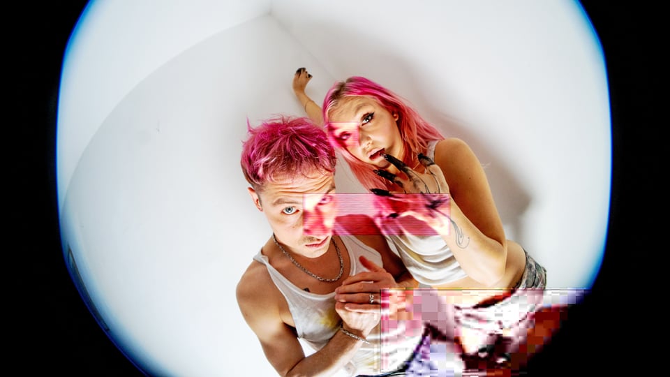 Zwei Personen mit pinken Haaren auf weißem Hintergrund, von oben fotografiert, mit starkem Weitwinkel und digitalen Glitch-Effekten.