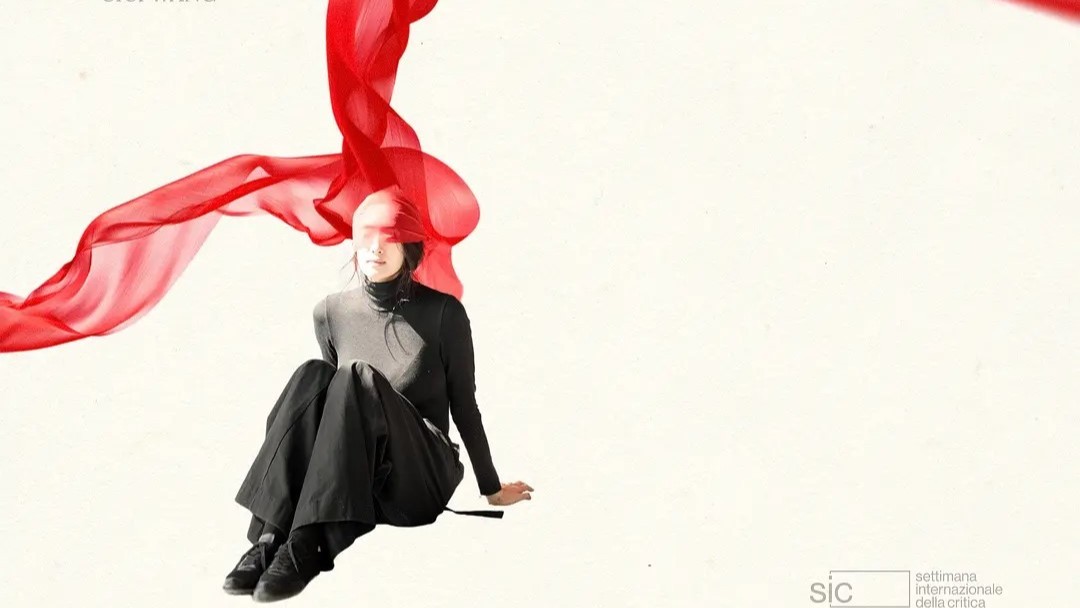 Person in schwarzer Kleidung vor hellem Hintergrund, über deren Kopf und Oberkörper sich ein leuchtend rotes, transparentes Stoffband windet zum dem Film A Dance In Vain