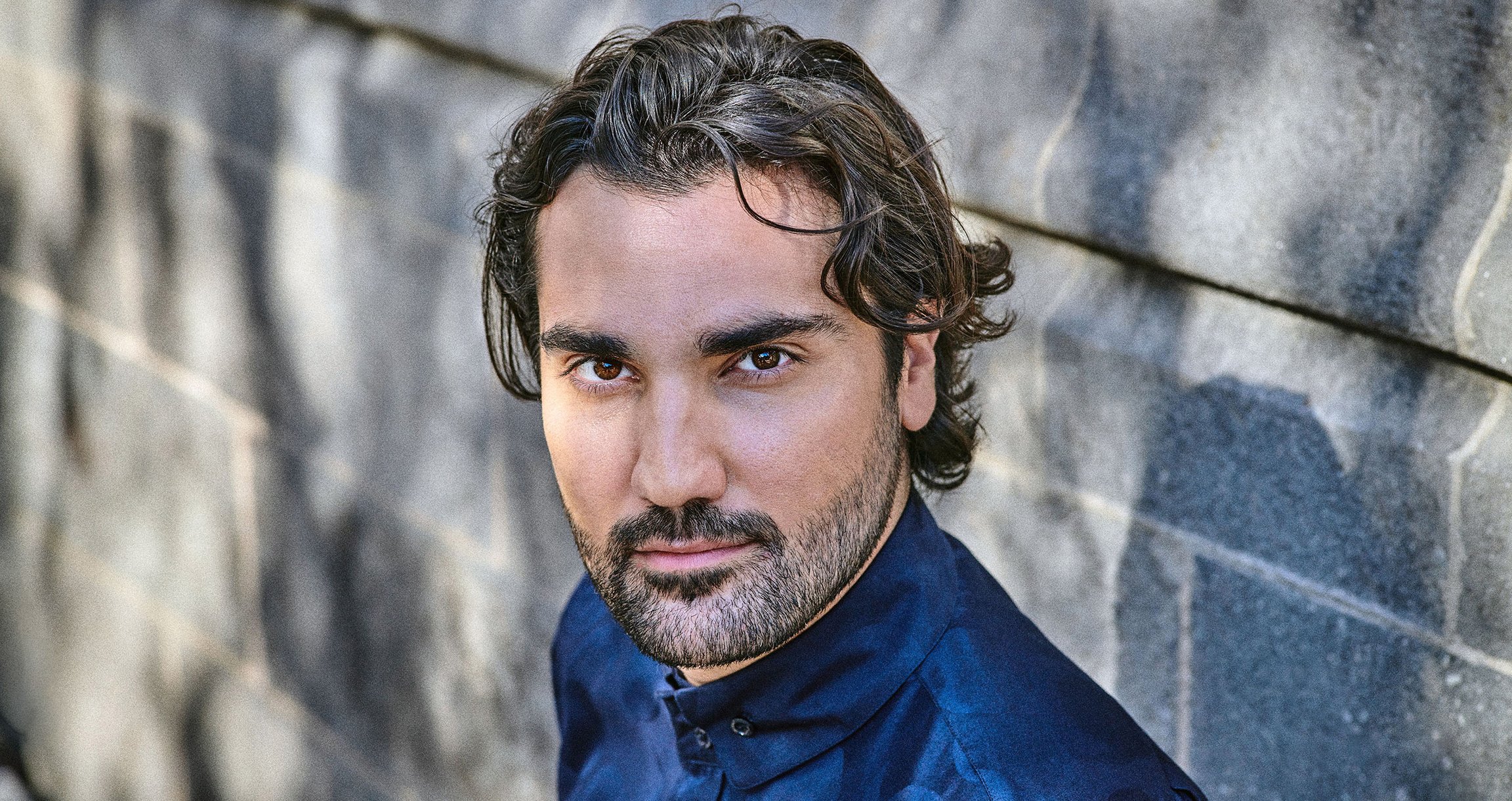 Portrait eines Mannes in blauem Hemd vor steinernem Hintergrund