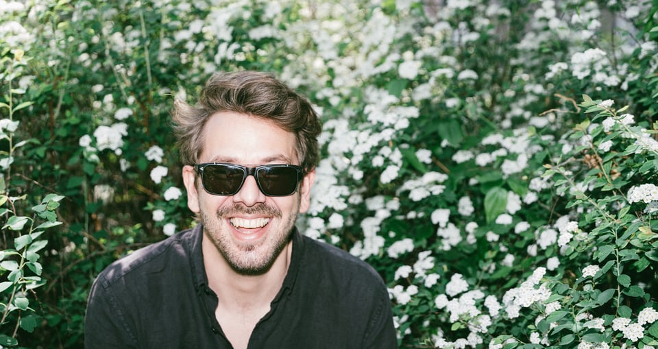 Foto des Künstlers mit Sonnenbrille und Blumen im Hintergrund