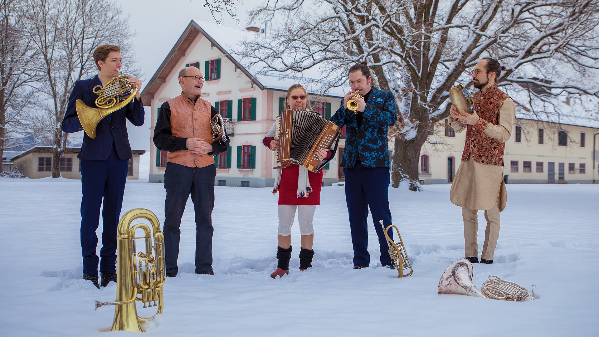 Fünf Personen in einer Schneelandschaft mit Blasinstrumenten, im Hintergrund ein traditionelles Bauernhaus