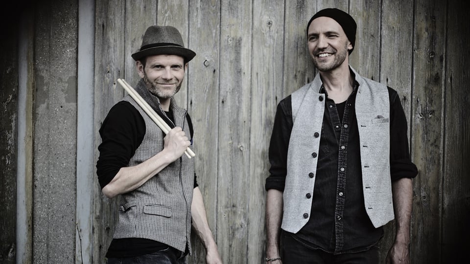 Foto zum Event von Double Drums: Die beiden Künstler lehnen an einer Holzwand