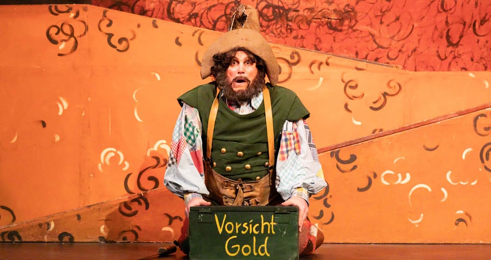 Der Darsteller des Räuber Hotzenplotz auf einer Bühne sitzend mit einer Kiste mit Aufschrift "Vorsicht Gold"