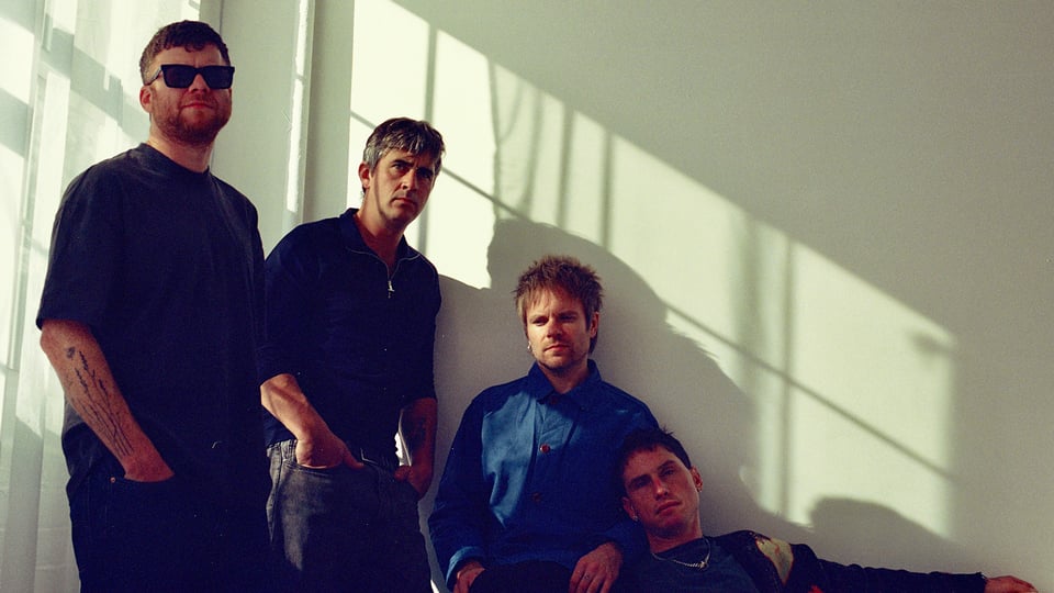 Foto für die Gruppe ENTER SHIKARI mit einem Bild der vier Künstler vor einer weißen Wand im Sonnenlicht.