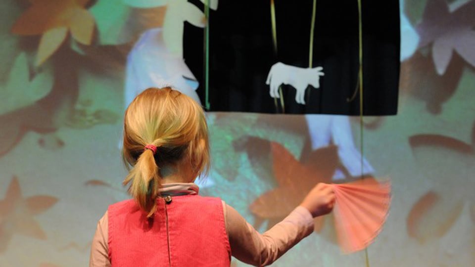 Ein Mädchen von Hinten mit einem Fächer in der Hand vor einer Zeichnung stehend