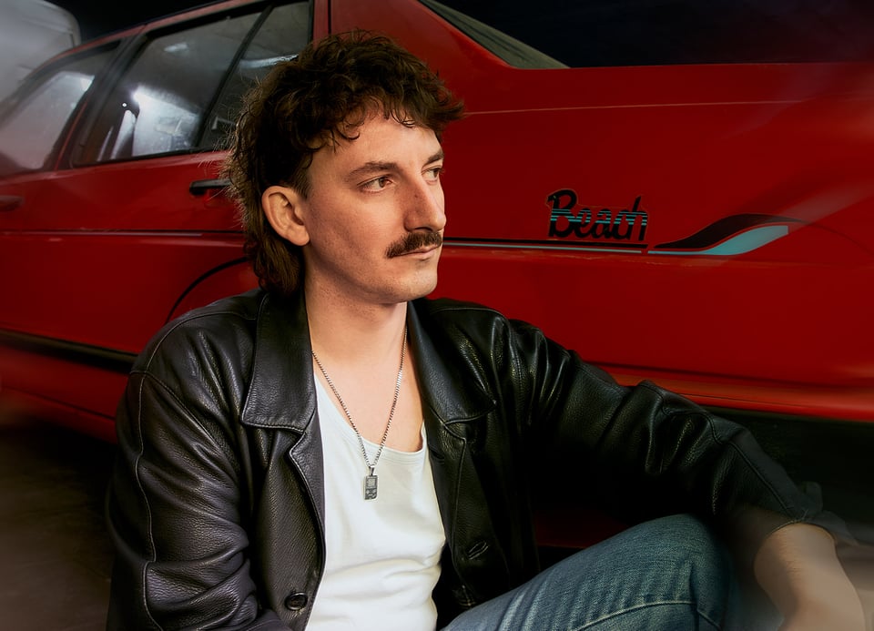 Foto des Künstlers mit einem roten Auto im Hintergrund
