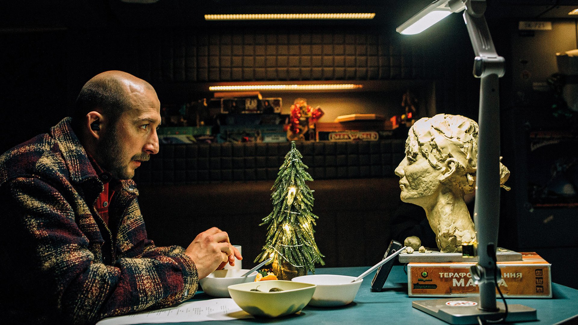 Foto für die Veranstaltung „Soloway 2026 – U are the Universe (Film)“ mit einem Mann am Tisch beim Essen und einem Statuenkopf ihm gegenüber.