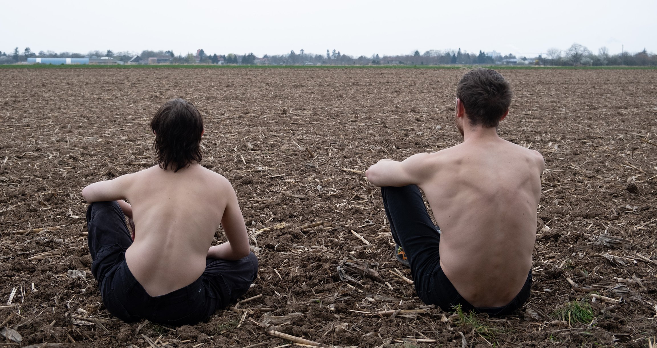2 Personen sitzen Oberkörperfrei auf einem Feld