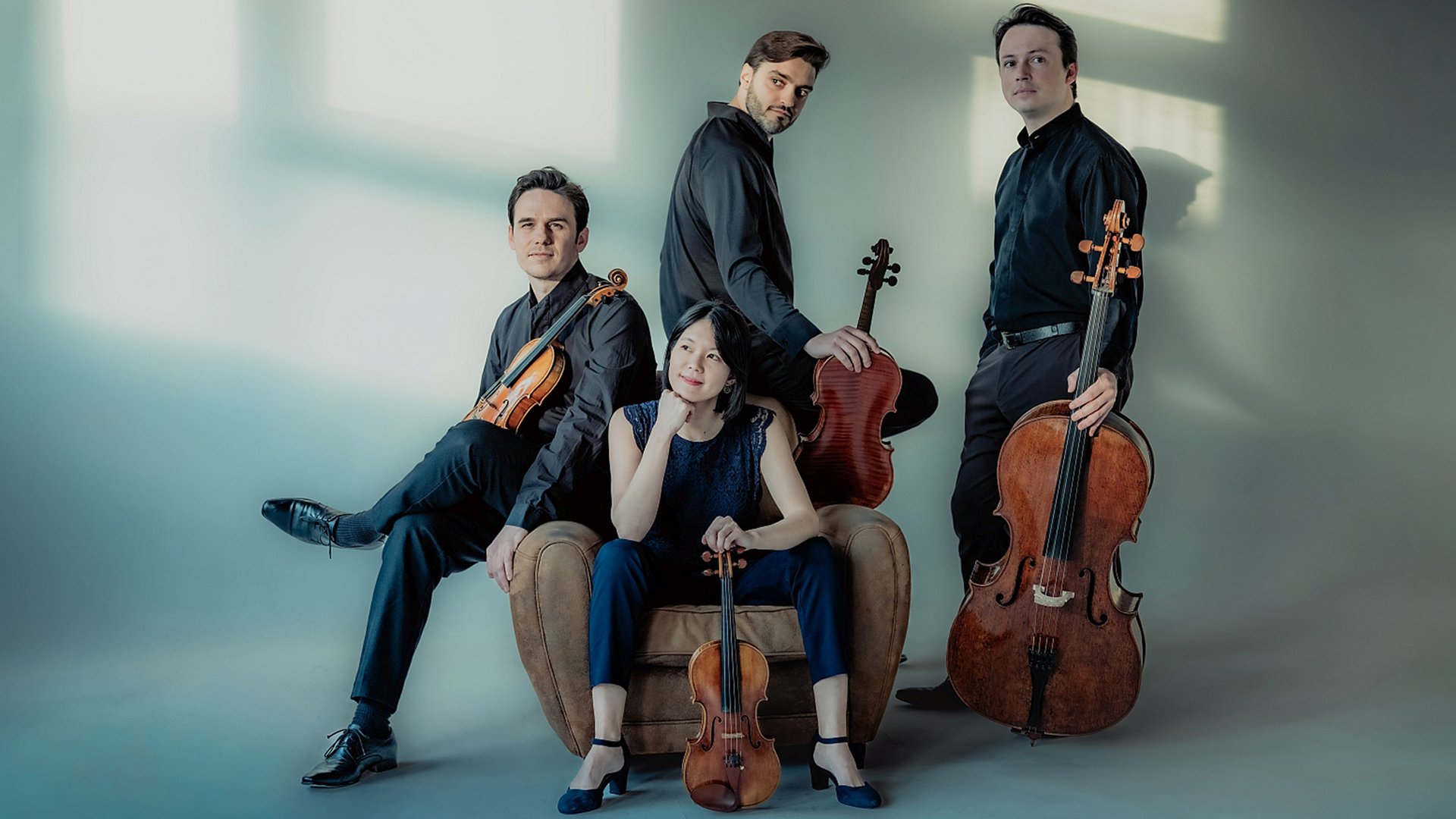 Vier Musiker mit Instrumenten, eine Musikerin sitz auf einem Sessel