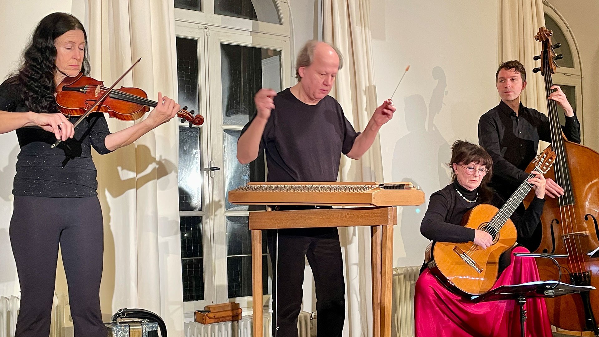 Neujahrskonzert Rudi Zapf & Freunde: Vier Musiker spielen Violine, Hackbrett, Gitarre und Kontrabass bei einem Konzert in einem Saal mit heller Innenraumkulisse.