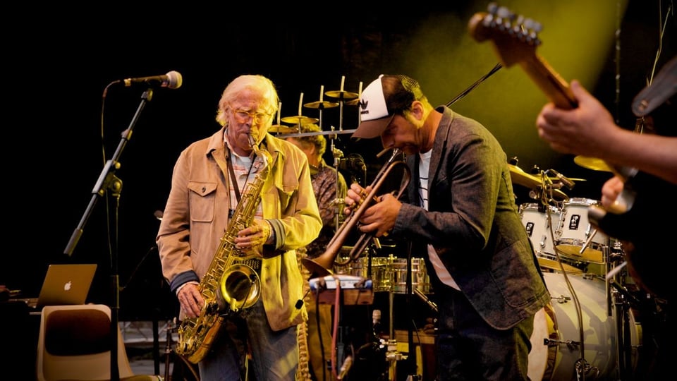 Klaus Doldinger sowie weitere Musiker der Band Passport mit Instrumenten auf der Bühne in warmem Licht
