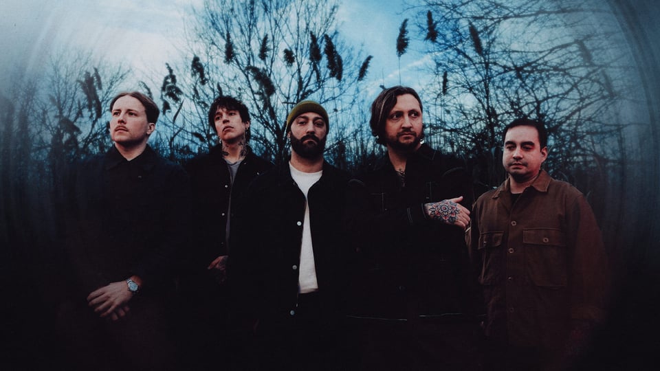 Fünf Personen von Erra and Currents dunkel gekleidet stehen nebeneinander im Freien in dichtem Abstand zueinander, Bäume und hohe Gräser im Hintergrund