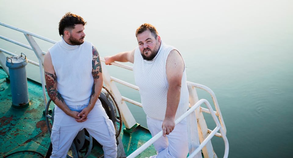 Zwei in weiß gekleidete Männer am Heck eines Schiffes stehend