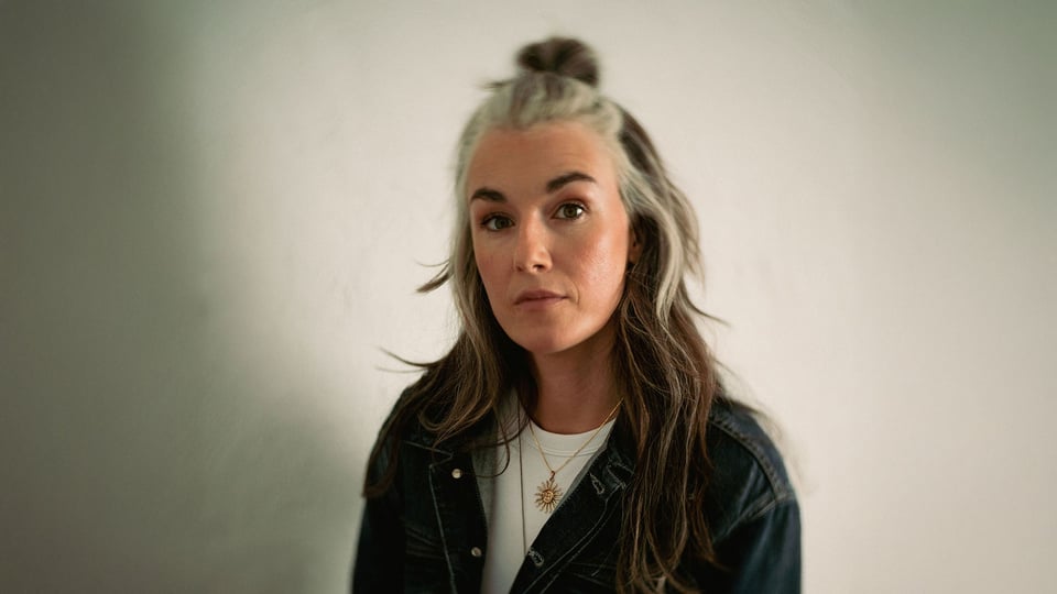 Foto für die Veranstaltung „Helena Delphi“ mit der Künstlerin vor hellem Hintergrund.