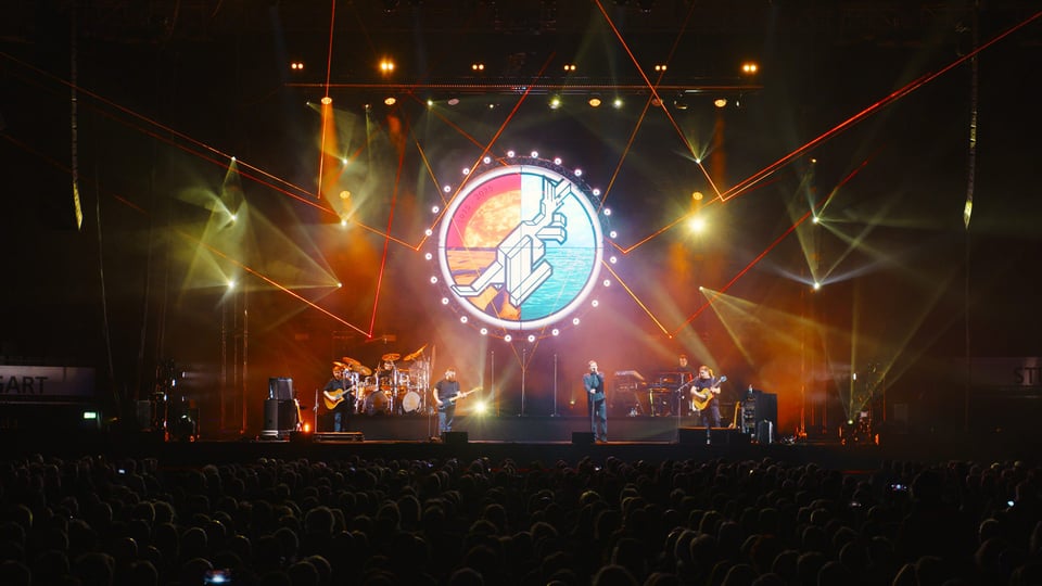 Die Musiker der Australian Pink Floyd Show auf der Bühne mit farbigem Licht und einem großen runden Logo
