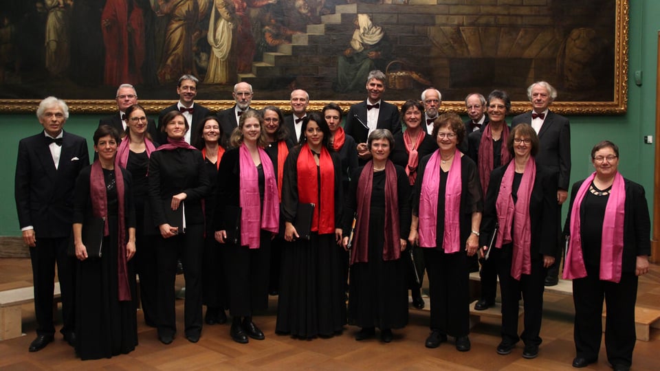 Zahlreiche Chormitgliedern in schwarzer Konzertkleidung und rosa und roten Schals vor einem großformatigen historischen Gemälde in einem Museums- oder Galerieraum