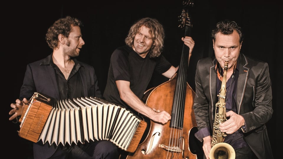 Die Band Quadro Nuevo mit Instrumenten in dunkler Kleidung vor dunklem Hintergrund