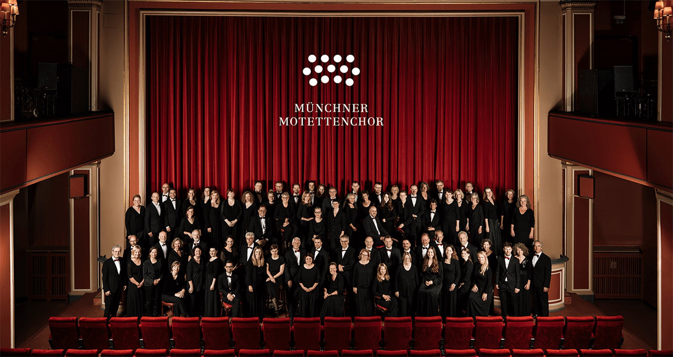 Der Münchner Motettenchor auf einer Bühne mit rotem Vorhang im Hintergrund