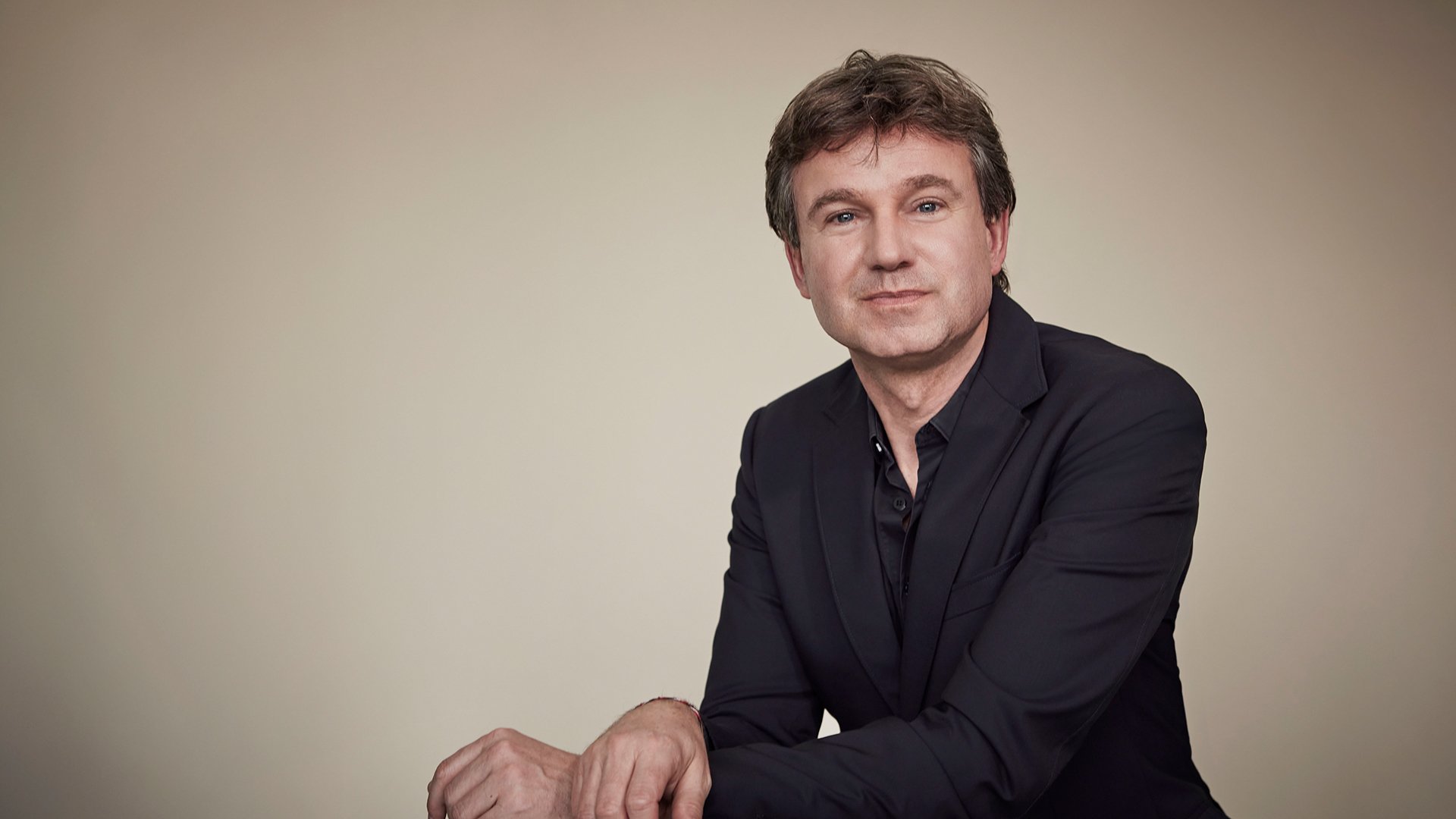 Ein Künstler in dunklem Anzug vor hellem Hintergrund