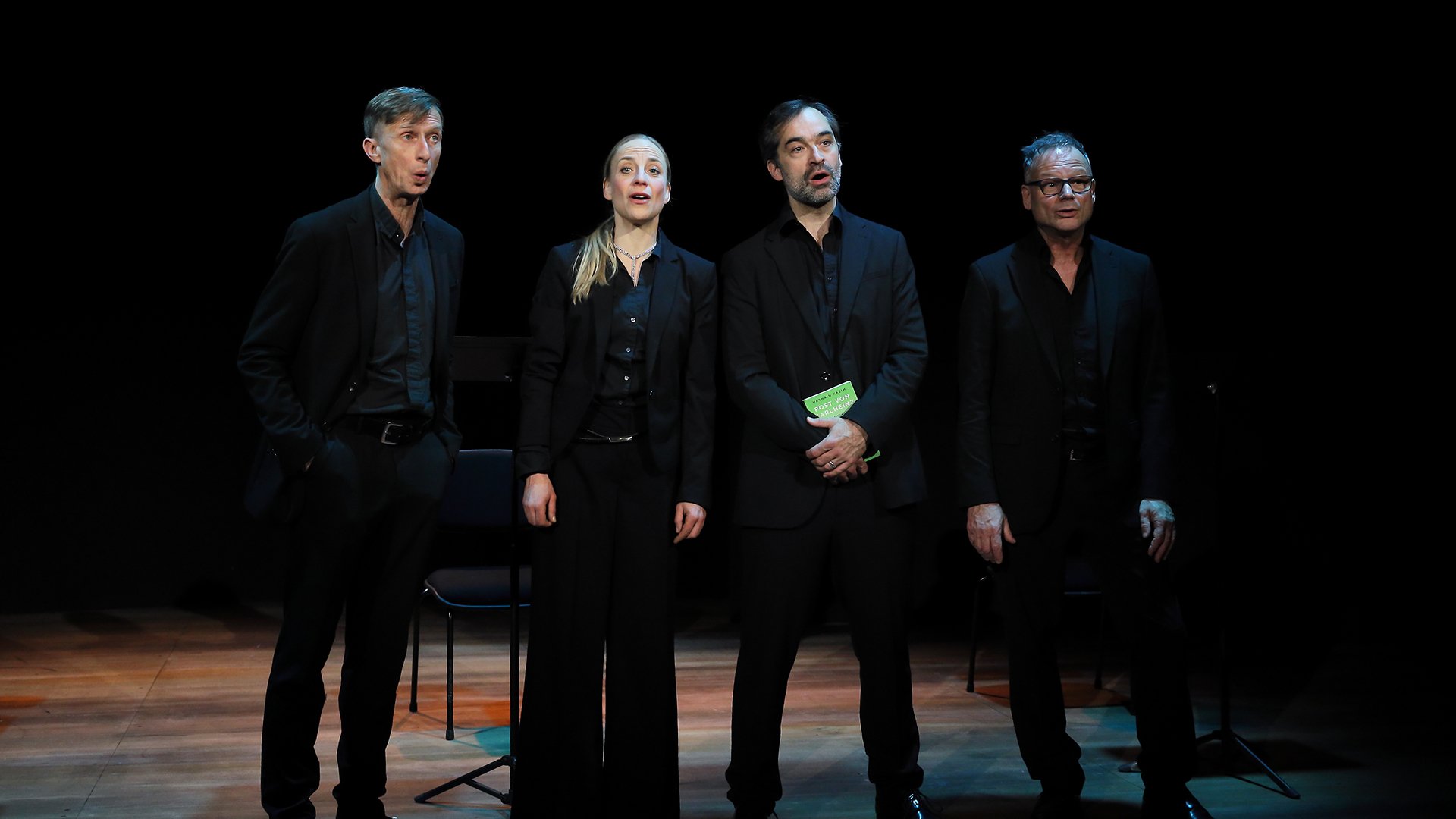 Vier Darsteller in schwarzer Kleidung auf einer Bühne
