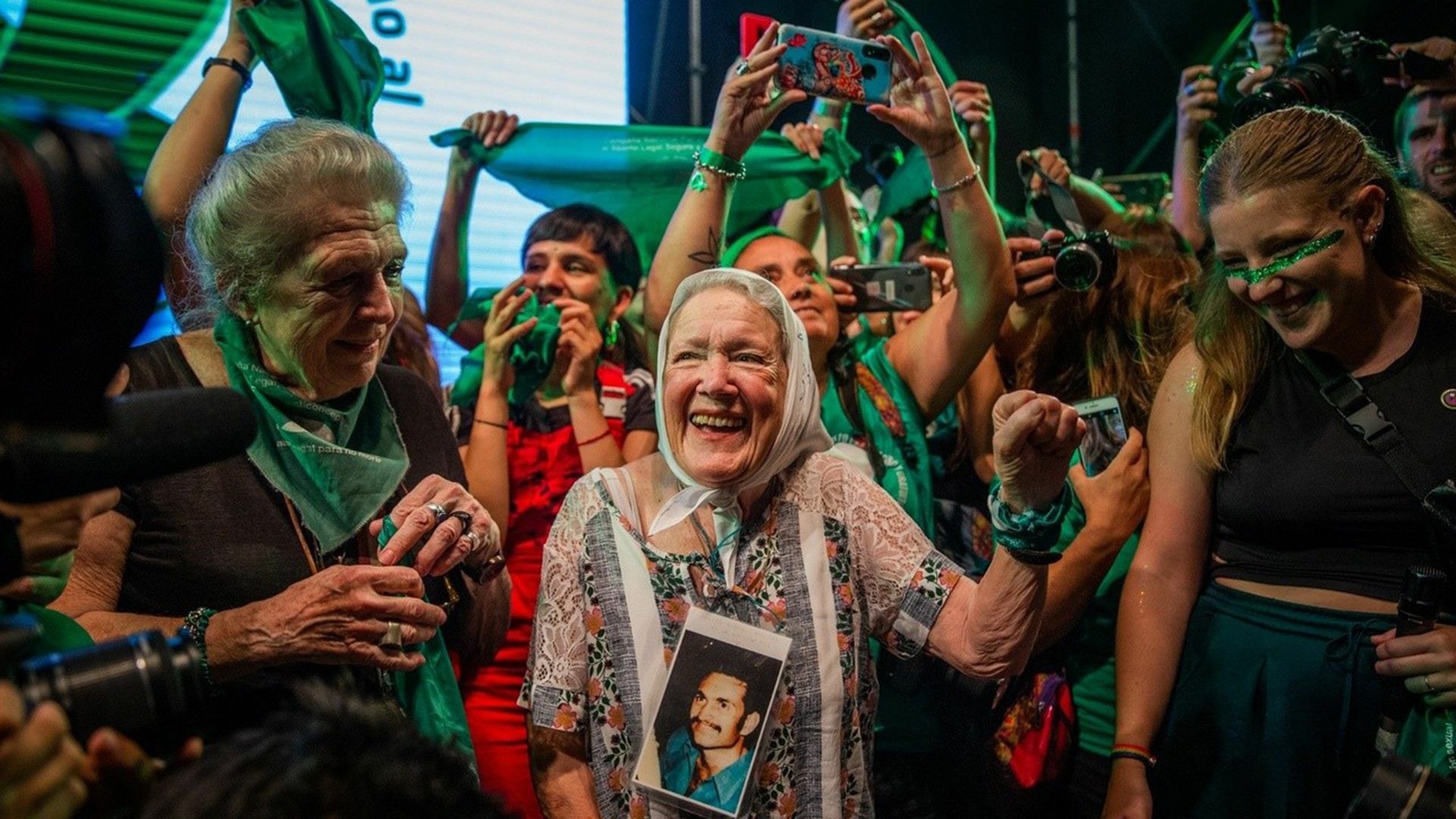 Foto für den Film ‚Norita‘, der zum LAFITA – Lateinamerikanische Filmtage München 2025 gehört, mit einer älteren Frau, die ein Foto eines Mannes in der Hand hält, und weiteren Personen, die um sie herum feiern