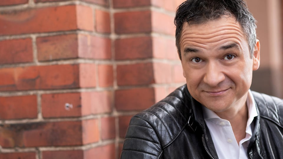 Foto für die Veranstaltung von Stephan Bauer mit dem Künstler in Lederjacke und einer Backsteinwand im Hintergrund