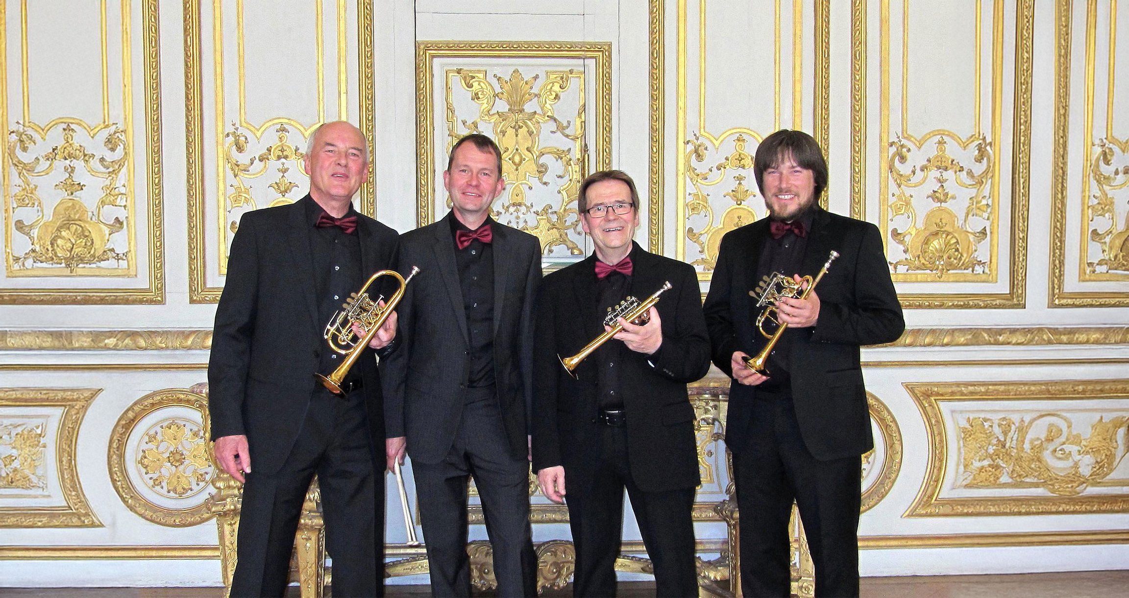 Vier Musiker in dunklen Anzügen mit Instrumenten