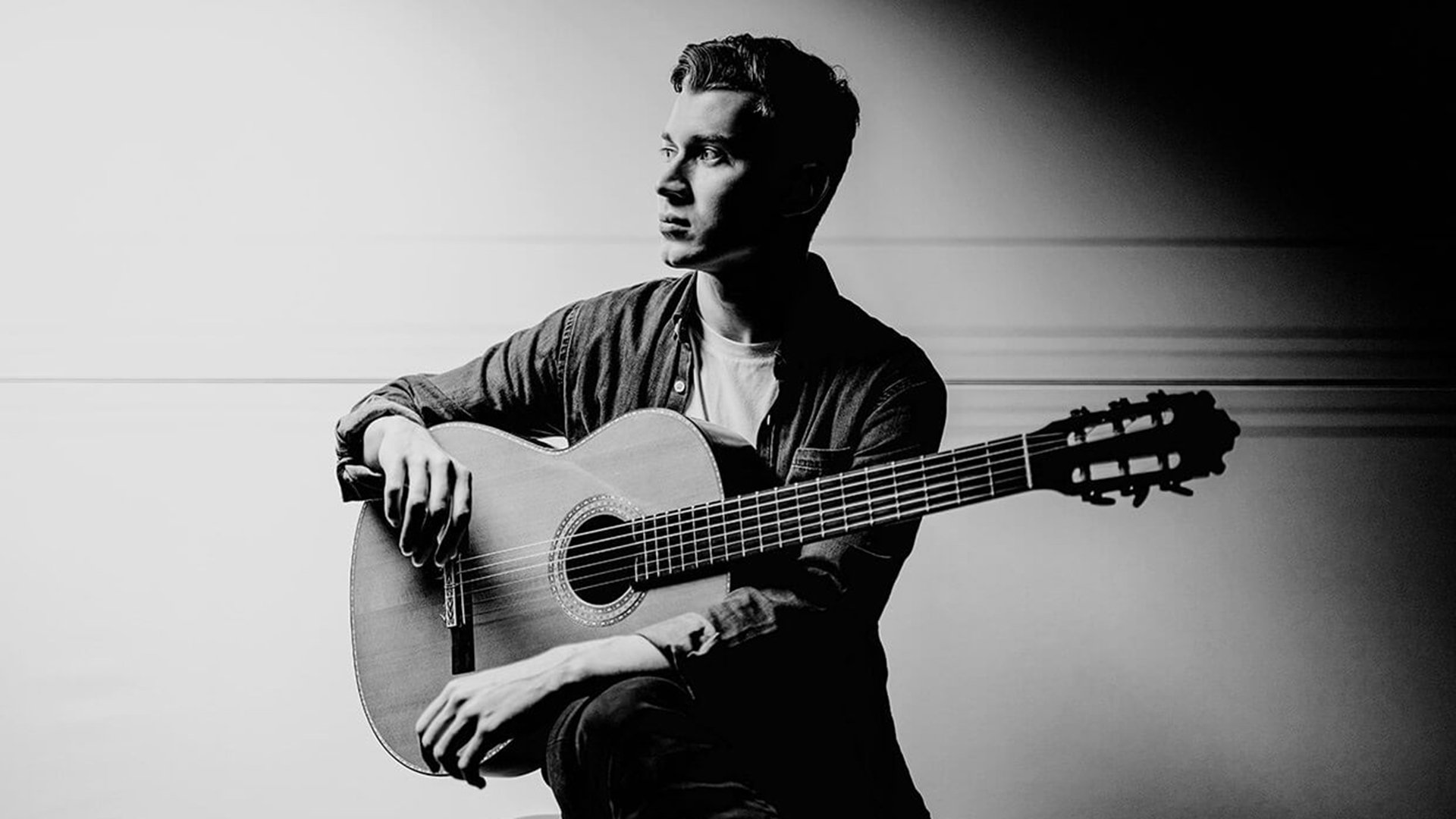 Schwarz-weiss Foto des Künstlers Thibaut Garcia mit Konzertgitarre, zur Seite blickend