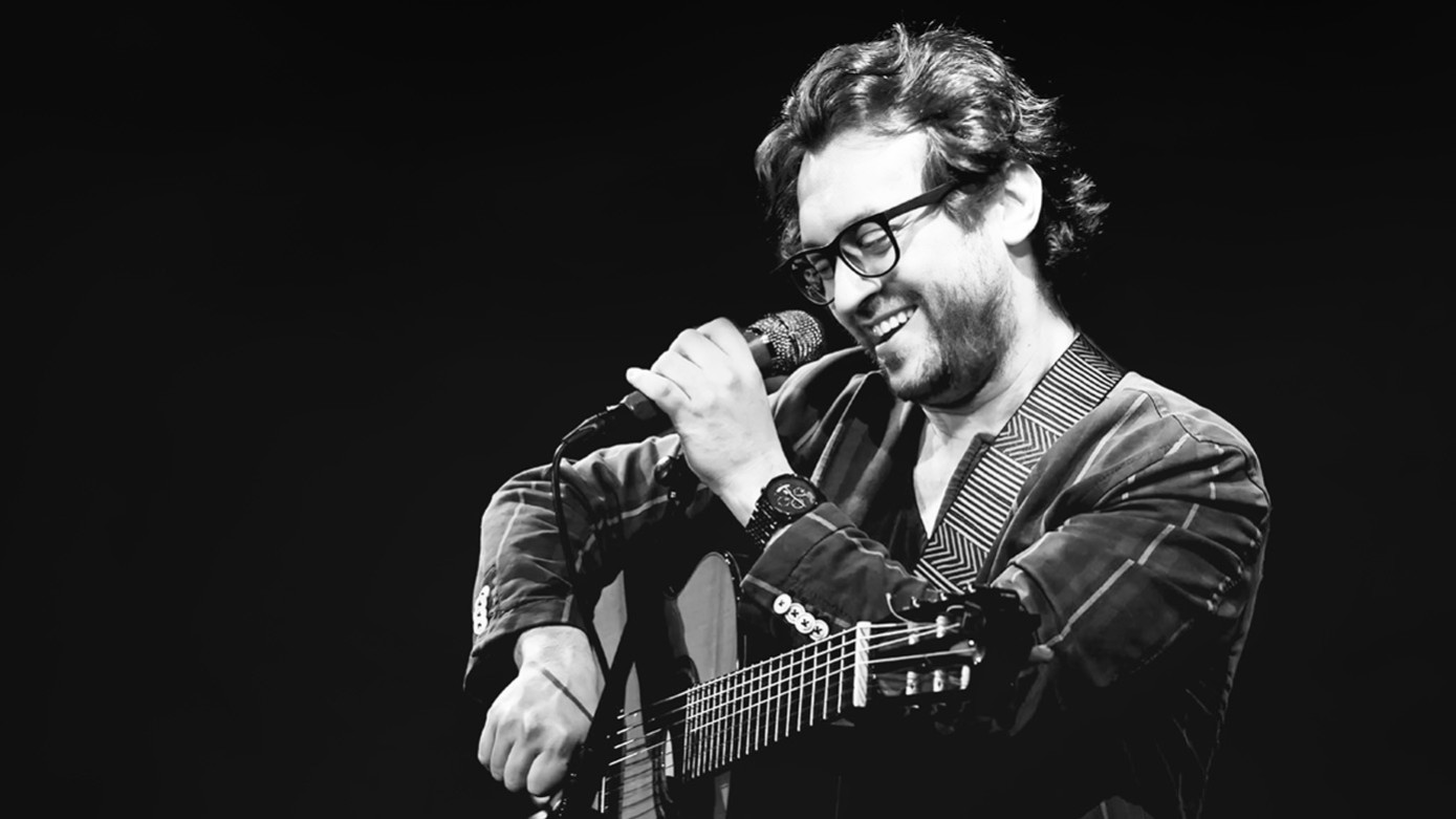 Schwarz-Weiß-Foto für die Veranstaltung von Mario Bakuna: Bossa Nova, mit dem Künstler am Mikrofon und mit einer Gitarre.