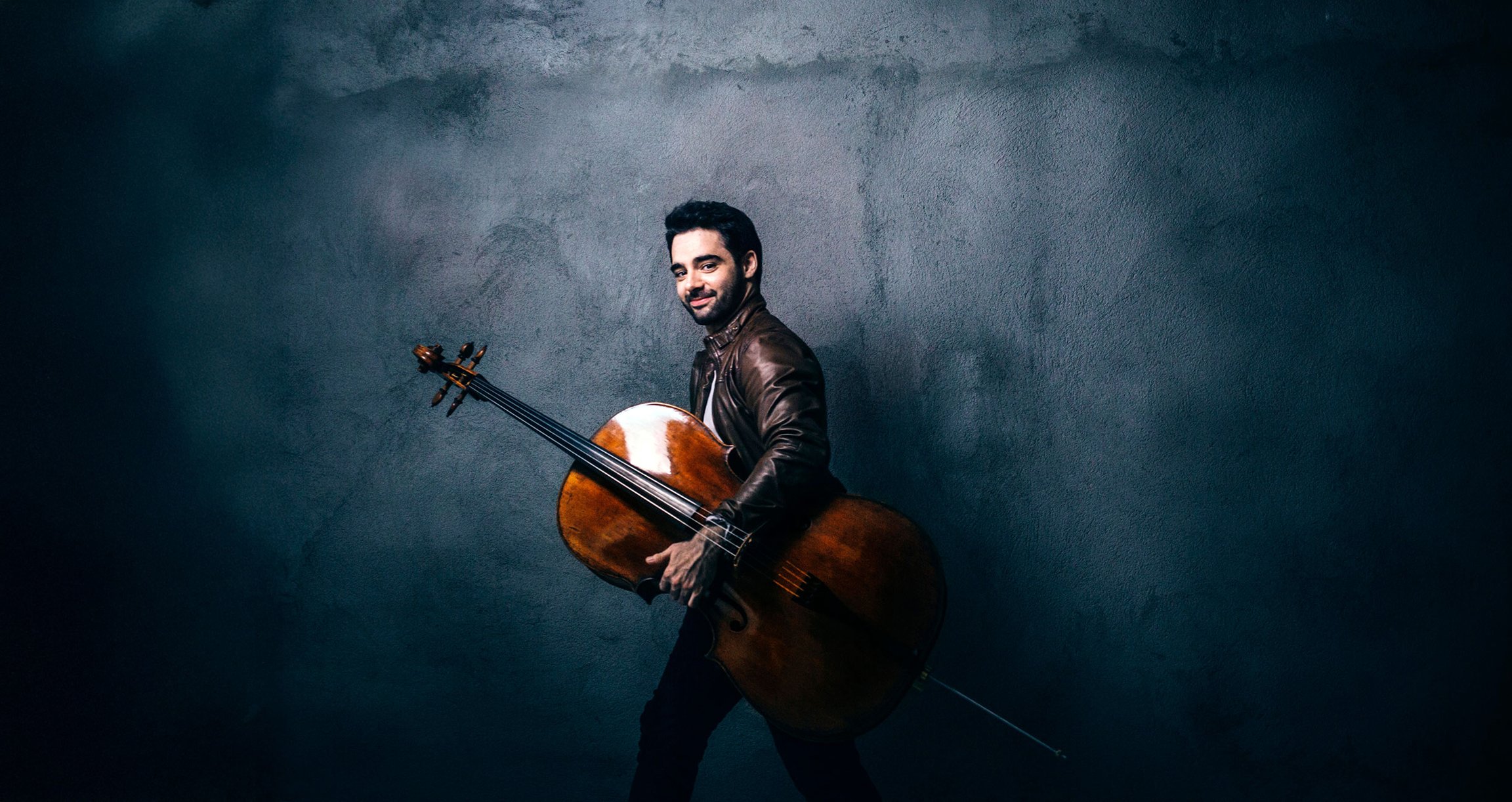 Pablo Ferrandez trägt sein Violoncello vor einem blauen Hintergrund
